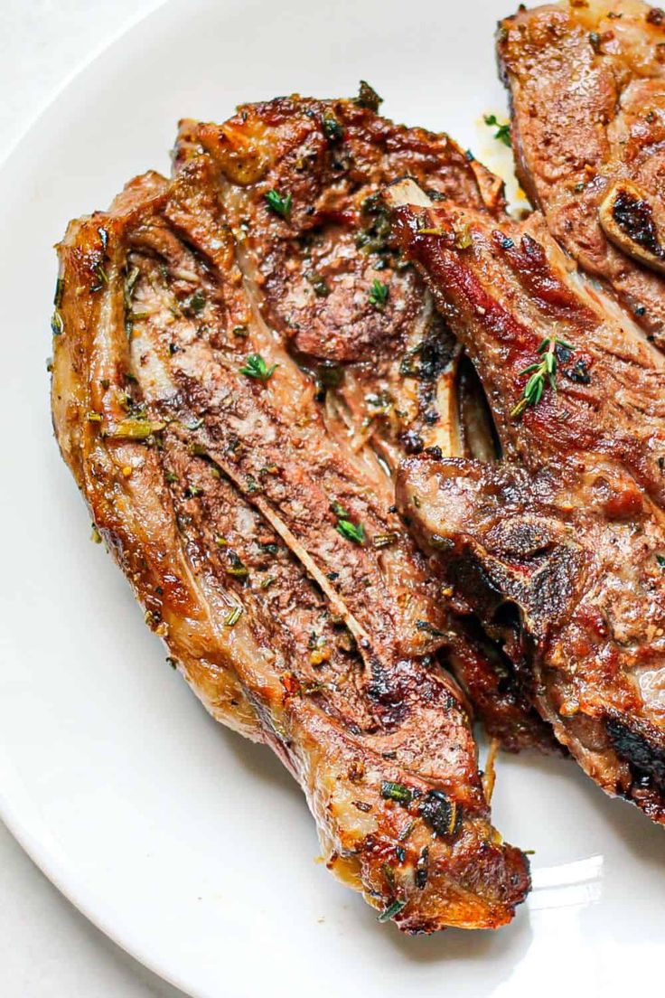 two steaks on a white plate with parsley and pepper garnishes