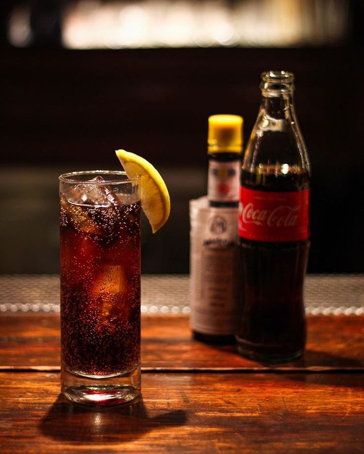 a glass filled with soda sitting on top of a wooden table next to two bottles