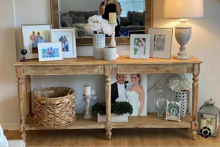 a wooden table topped with pictures and vases filled with flowers next to a mirror