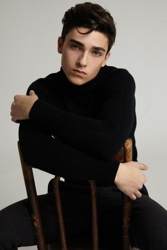 a young man sitting in a chair with his arms crossed and looking at the camera