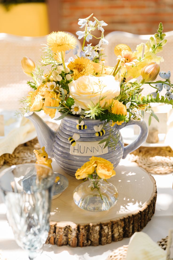 A yellow, white, and blue flower arrangement in a blue Winnie the pooh ceramic teapot on a large tree slice at a baby shower Baby Shower Center Piece, Baby Shower Center, Hunter Photography, Honey Bee Baby Shower, Winnie The Pooh Baby Shower, Baby Shower Theme Decorations, Baby Shower Yellow, Disney Baby Shower, Bee Baby Shower Theme