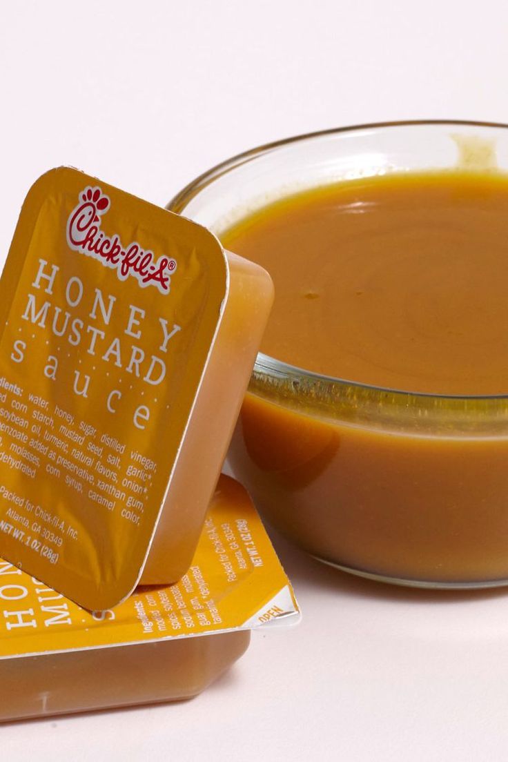 a bowl of honey mustard sauce next to two packets of buttered hot sauce on top of them