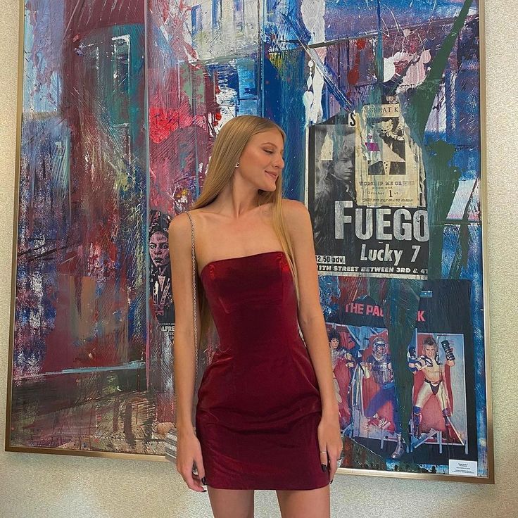 a woman standing in front of a painting wearing a red dress and high heeled boots