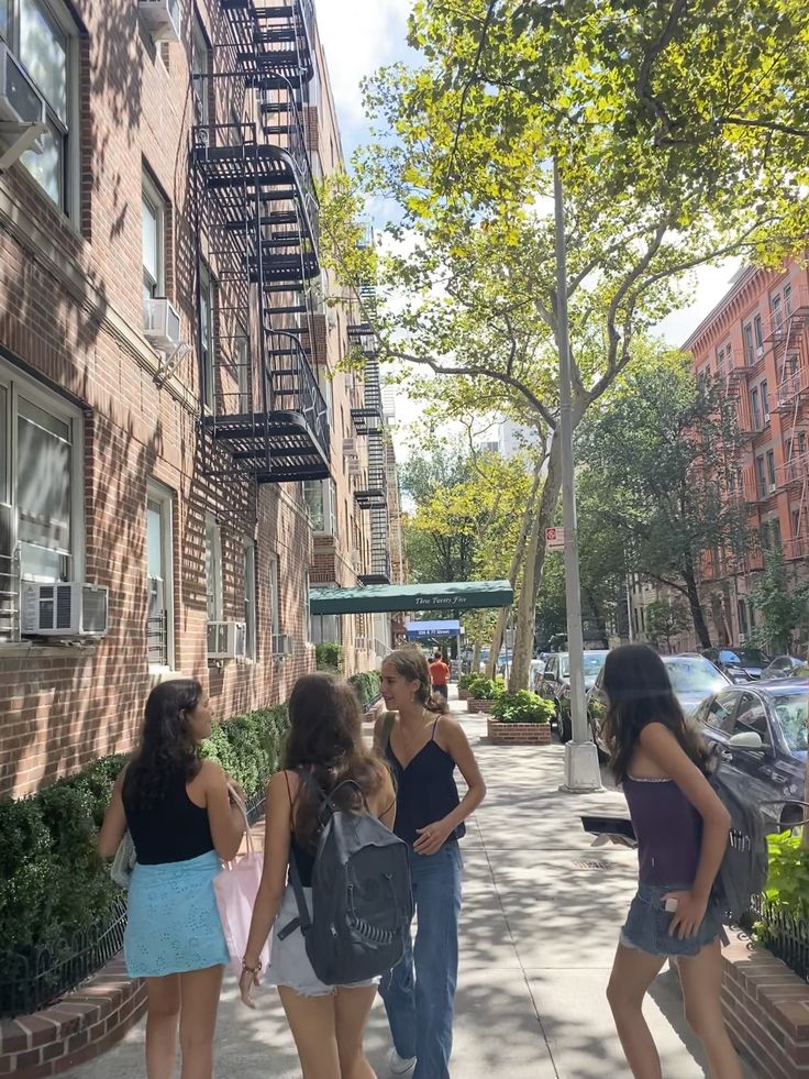 four girls are standing on the sidewalk talking to each other