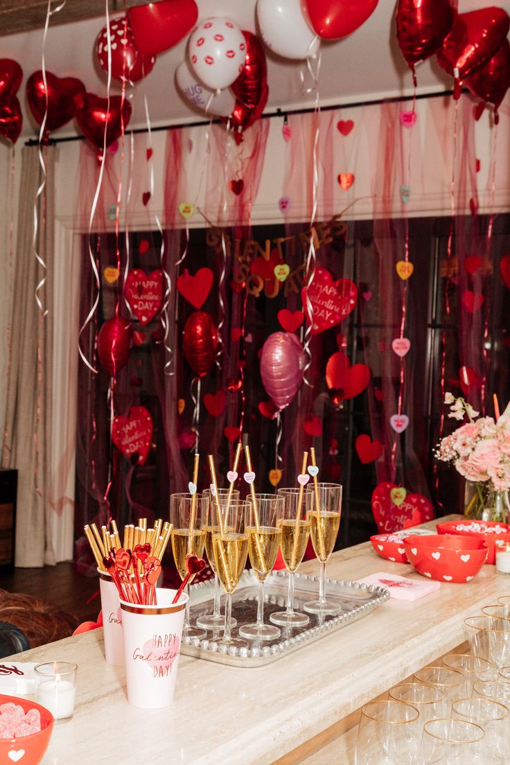 a table topped with lots of wine glasses filled with champagne and heart shaped balloons hanging from the ceiling