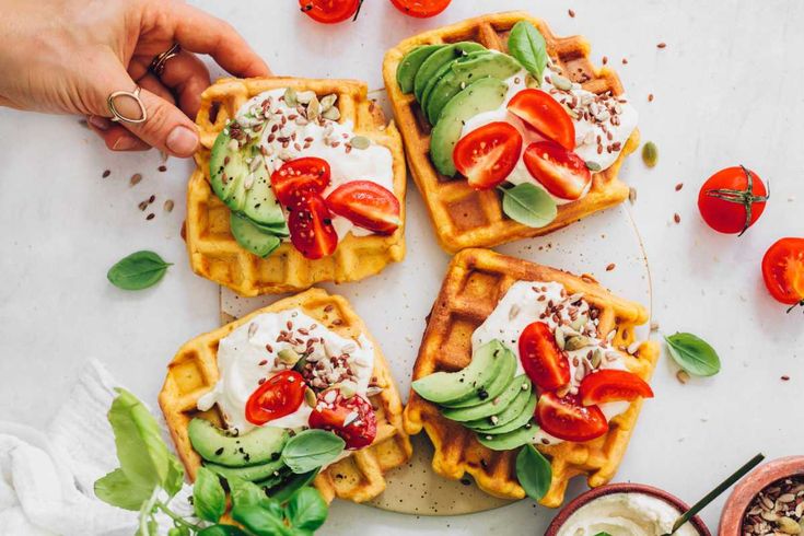 four waffles topped with avocado, tomatoes and cucumbers