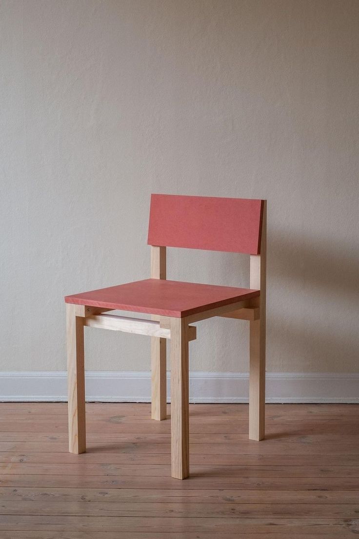 a red chair sitting on top of a hard wood floor next to a white wall