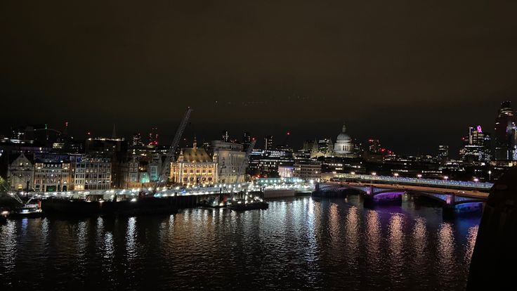 the city skyline is lit up at night with lights reflecting in the water and buildings on both sides