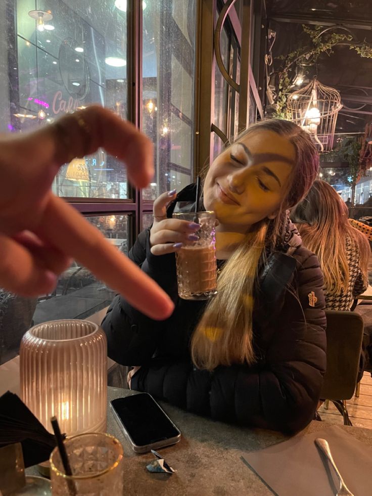 a woman is sitting at a table with her face painted like a doll and holding a drink