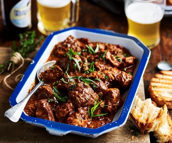 a blue bowl filled with meat next to bread and beer