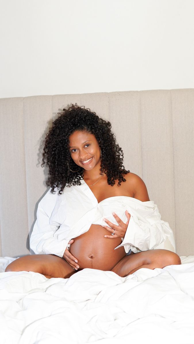 a pregnant woman sitting on top of a bed with her belly wrapped in a blanket