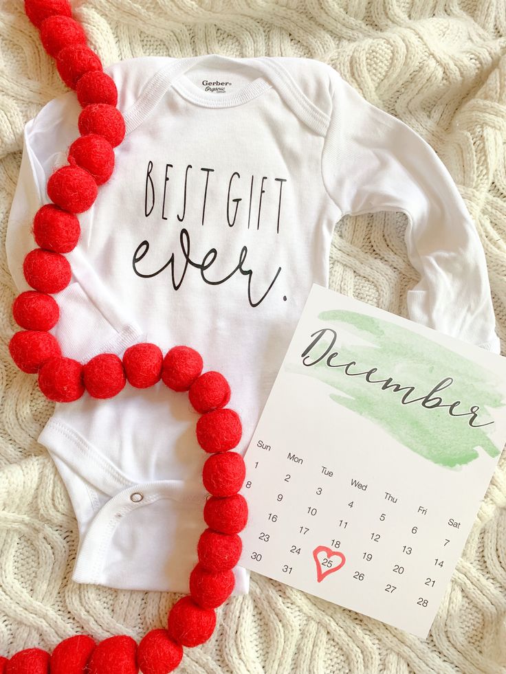 a baby's bodysuit and red pom - poms are laying on a blanket