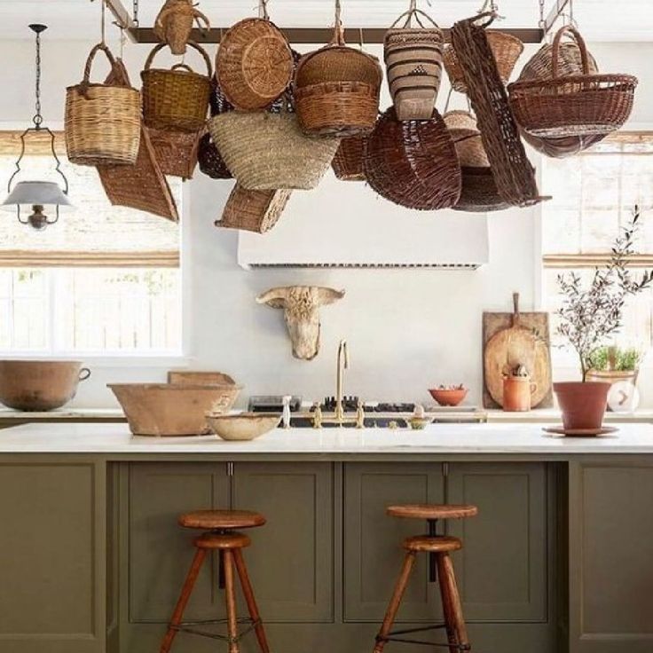 baskets hanging from the ceiling in a kitchen with stools next to it and an island