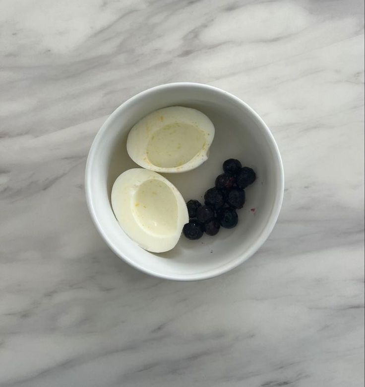 two peeled bananas and some blackberries in a white bowl on a marble countertop