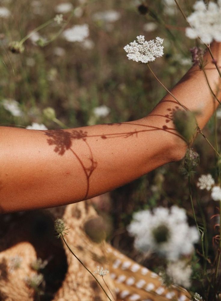 a woman's arm with vines on it and white flowers in the foreground