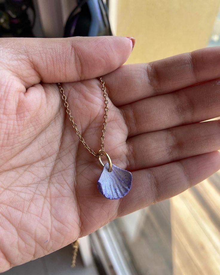 a hand holding a tiny blue shell on a gold chain