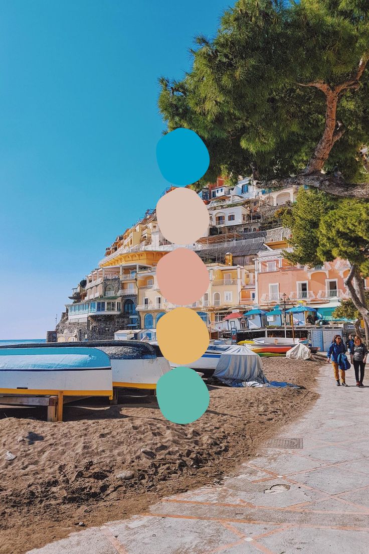 people walking on the beach next to boats and houses with colorful circles hanging from them