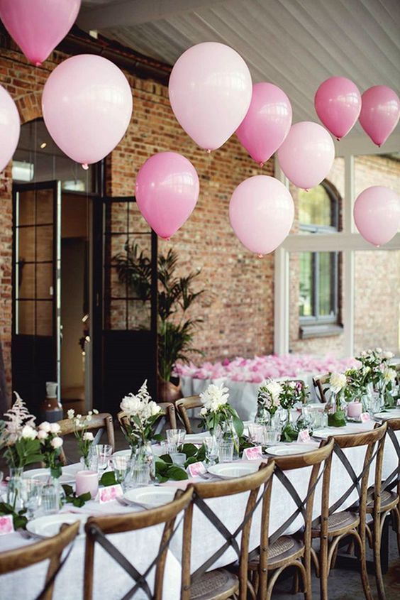 an image of a table set up for a party with pink and white balloons hanging from the ceiling