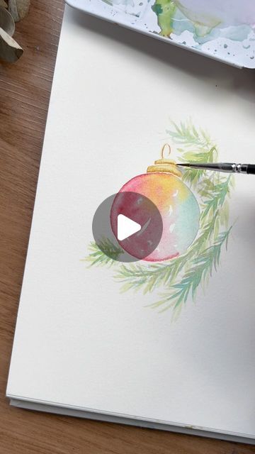 someone is painting a christmas ornament on a piece of paper with watercolors