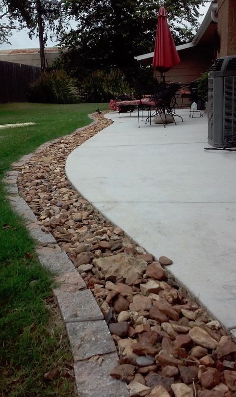 a patio area with rocks, grass and an umbrella