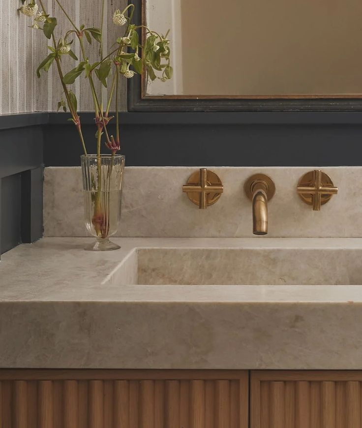 a bathroom sink with two gold faucets and a vase full of flowers on the counter