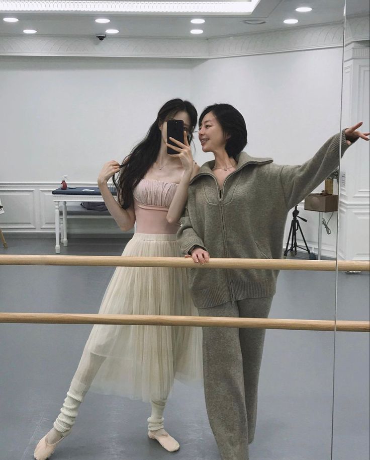 two women standing next to each other in front of a ballerina's mirror