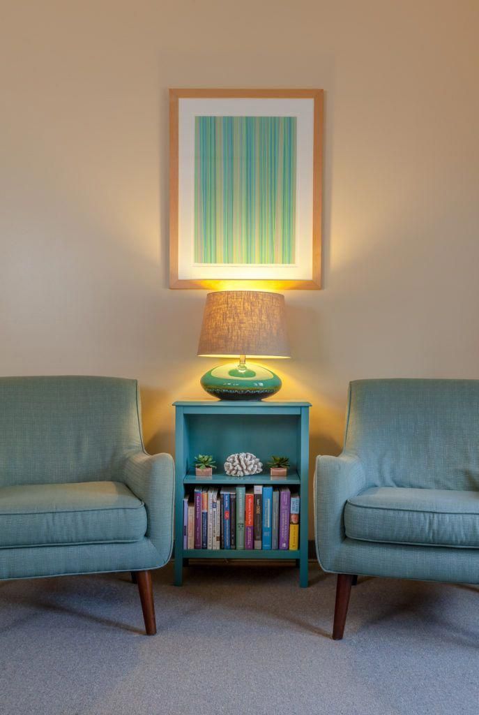 two blue chairs sitting next to each other in front of a table with a lamp on it