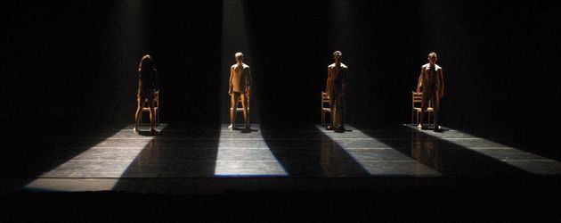 four wooden mannequins standing in the dark with their shadows cast on them