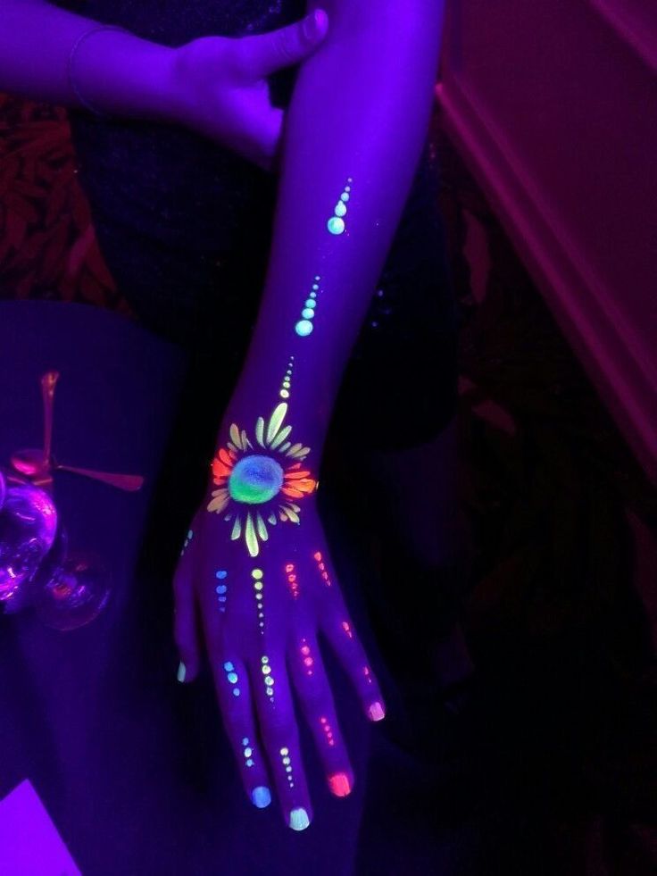 a woman's arm with glow paint on it and flowers painted on her hands