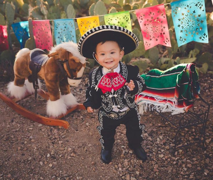 a little boy wearing a sombrero and standing next to a rocking horse in the dirt