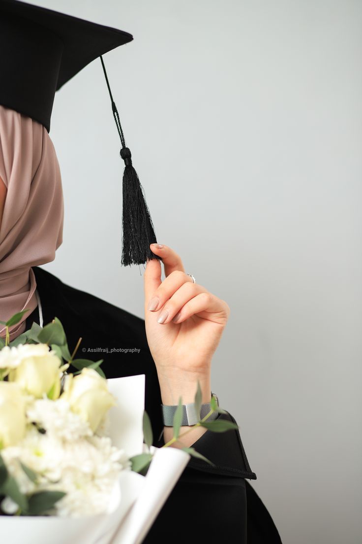 a woman in a black graduation gown holding a bouquet of flowers and a tassel