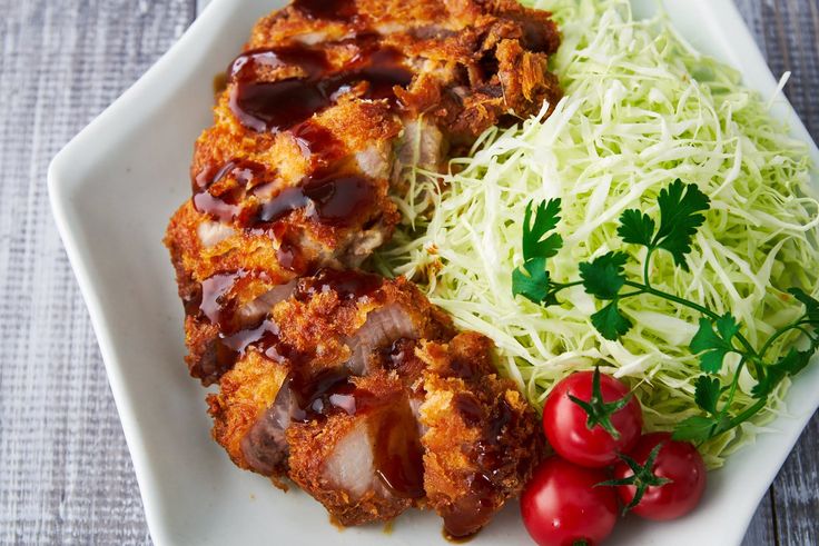 a white plate topped with meat covered in sauce next to veggies and tomatoes