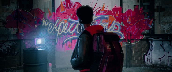 a person standing in front of a wall with graffiti on it and holding a backpack