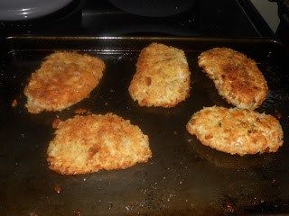 six fried chicken patties on a baking sheet ready to be cooked in the oven