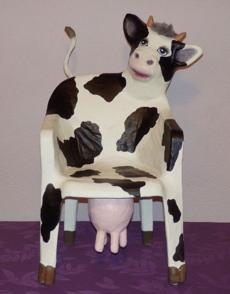 a toy cow sitting on top of a plastic chair with its legs crossed and eyes wide open