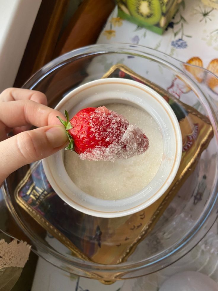 a person is holding a strawberry in a bowl