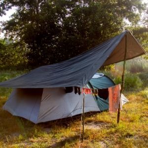 a tent pitched up in the middle of a field with trees and grass around it