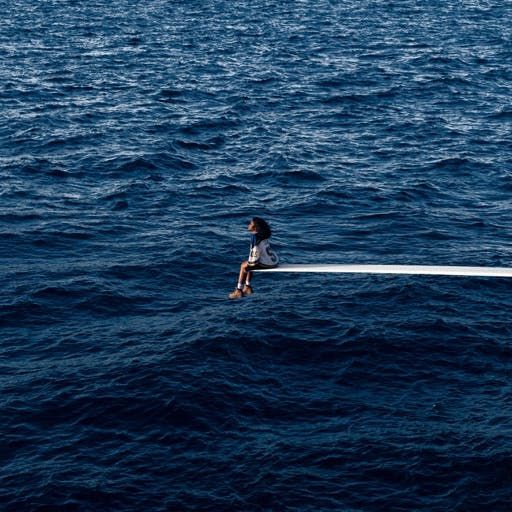 a person sitting on top of a boat in the middle of the ocean with their legs crossed