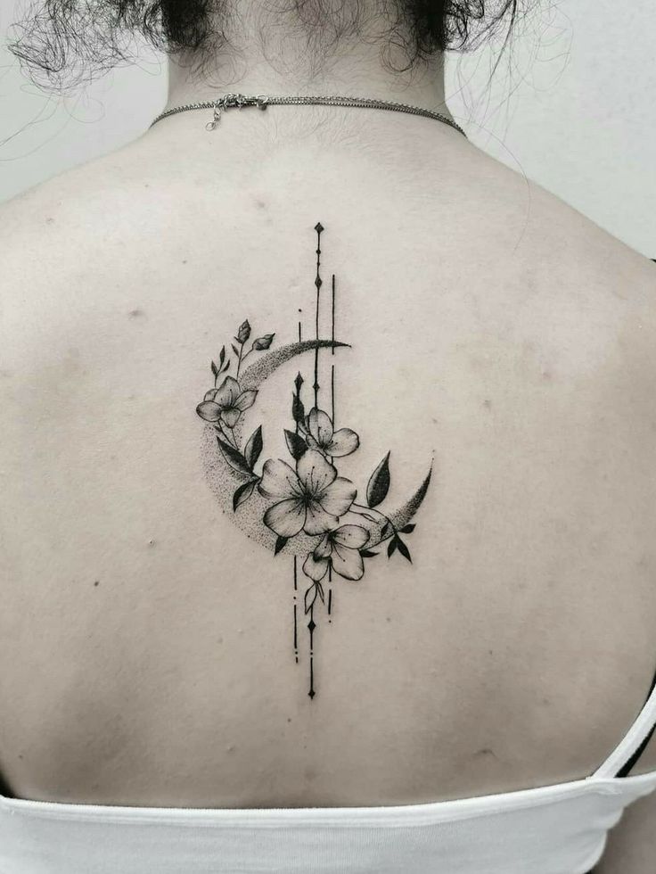 the back of a woman's shoulder with flowers and an arrow tattoo on it