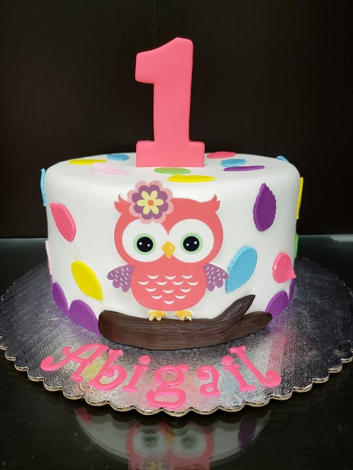 a birthday cake decorated with an owl and pink number one on the top, sitting on a glass plate