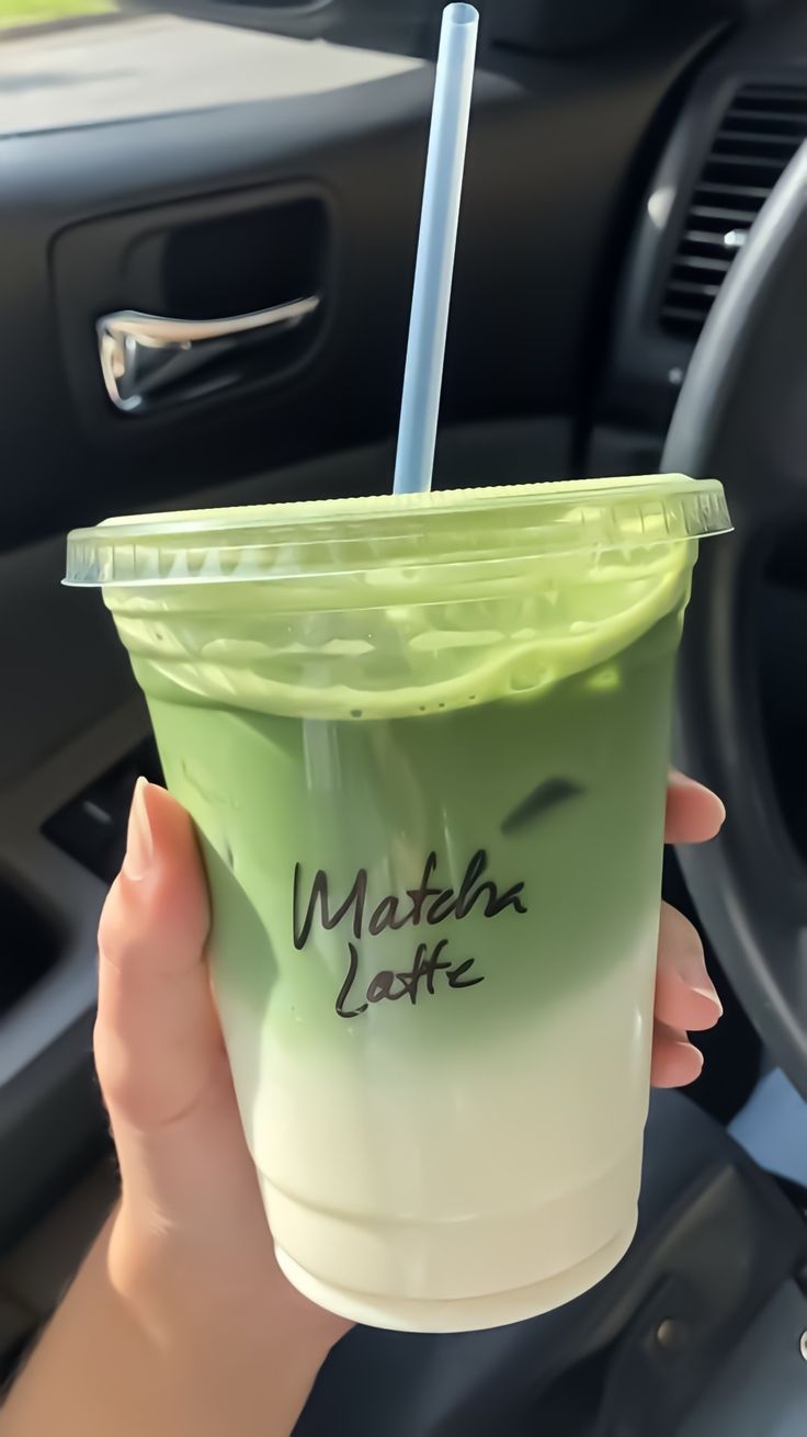 a person holding up a green drink with a straw in it's hand while sitting in the driver's seat of a car