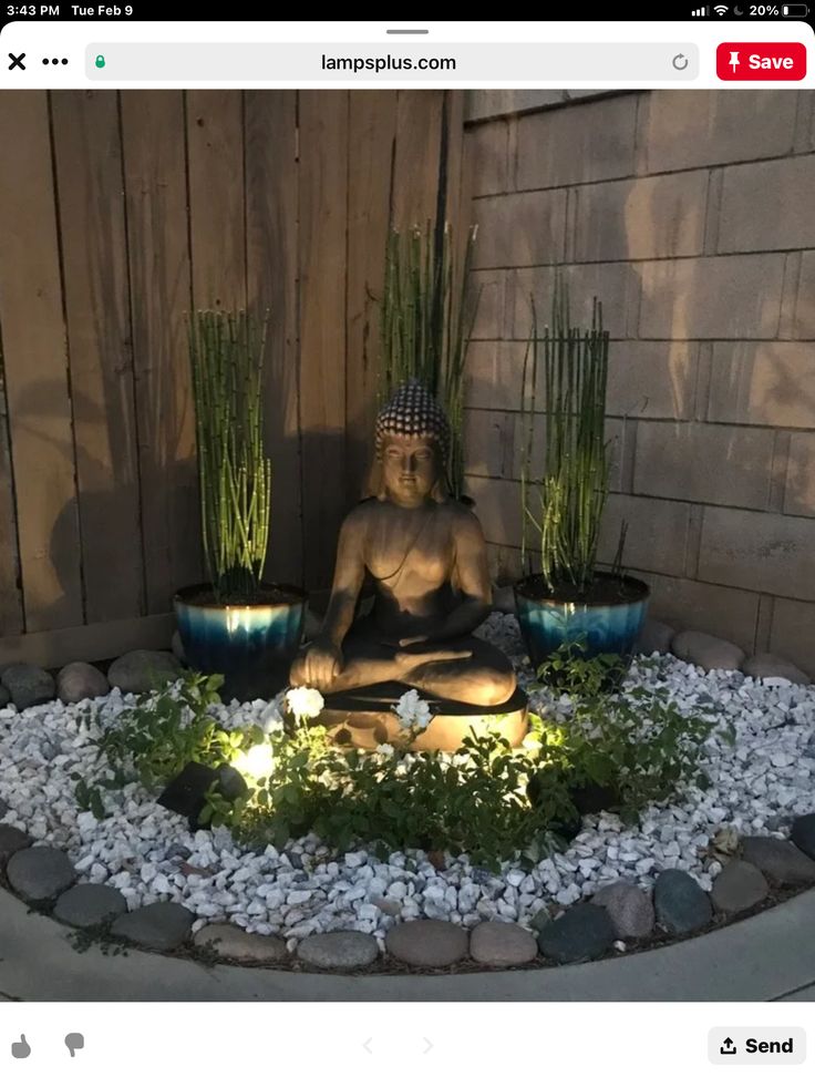 a buddha statue sitting in the middle of a garden with plants and rocks around it