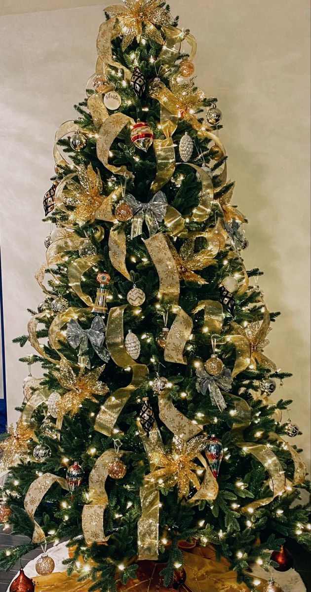 a decorated christmas tree with gold and silver ribbons on it's top, in a living room