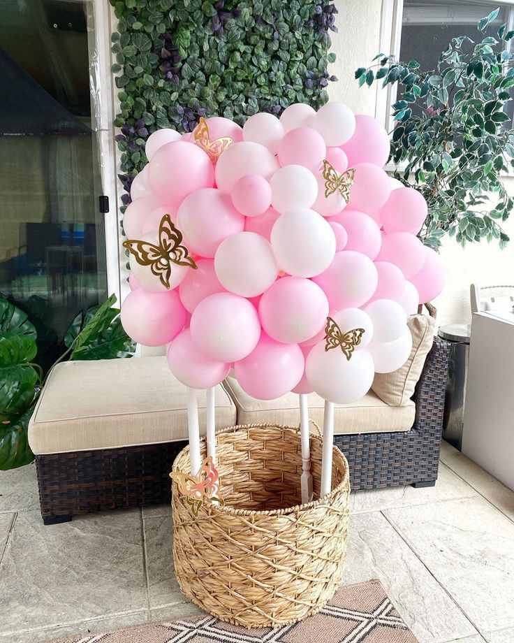 pink and white balloons are in a basket on the ground next to a planter