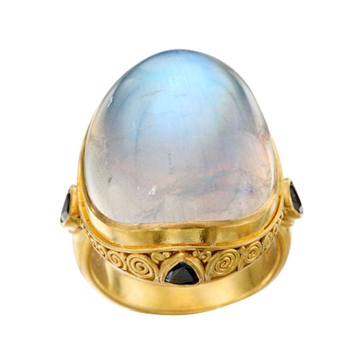 A signature classic Steven Battelle cocktail ring with a huge 19 x 24 mm shimmering oval rainbow blue moonstone cabochon and a carat of trillium faceted blue sapphires set in a handmade ancient-inspired "spirals and jawan" 18K gold setting. Rainbow moonstone is believed to help strengthen intuition and psychic perception, especially offering us visions of things that aren't immediately obvious. This ring is a SHOWSTOPPER that will be commented on by everyone who sees it. Currently sized 7, this Strengthen Intuition, Spinel Jewelry, 22k Gold Ring, Sapphire Cocktail Ring, Gold For Sale, Gold Cocktail Ring, Blue Moonstone, Rainbow Moonstone Ring, Grey Diamond