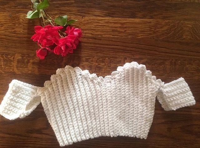 a white knitted sweater next to a red flower on a wooden table with wood flooring