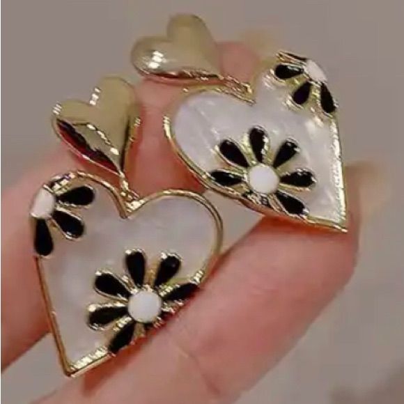 two heart shaped brooches with black and white flowers on them are held in someone's hand