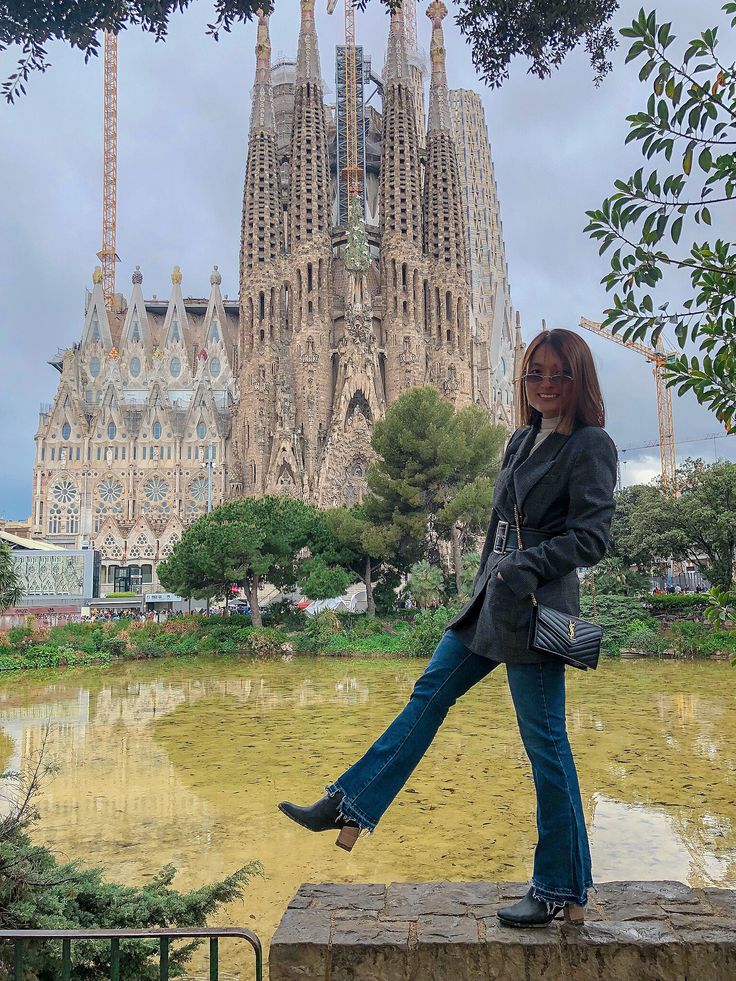 a woman standing on top of a stone wall next to a large building with spires