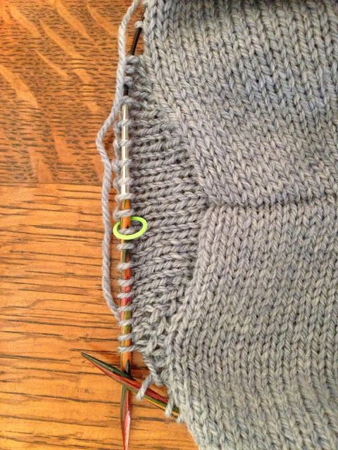 an open knitted bag sitting on top of a wooden table next to knitting needles