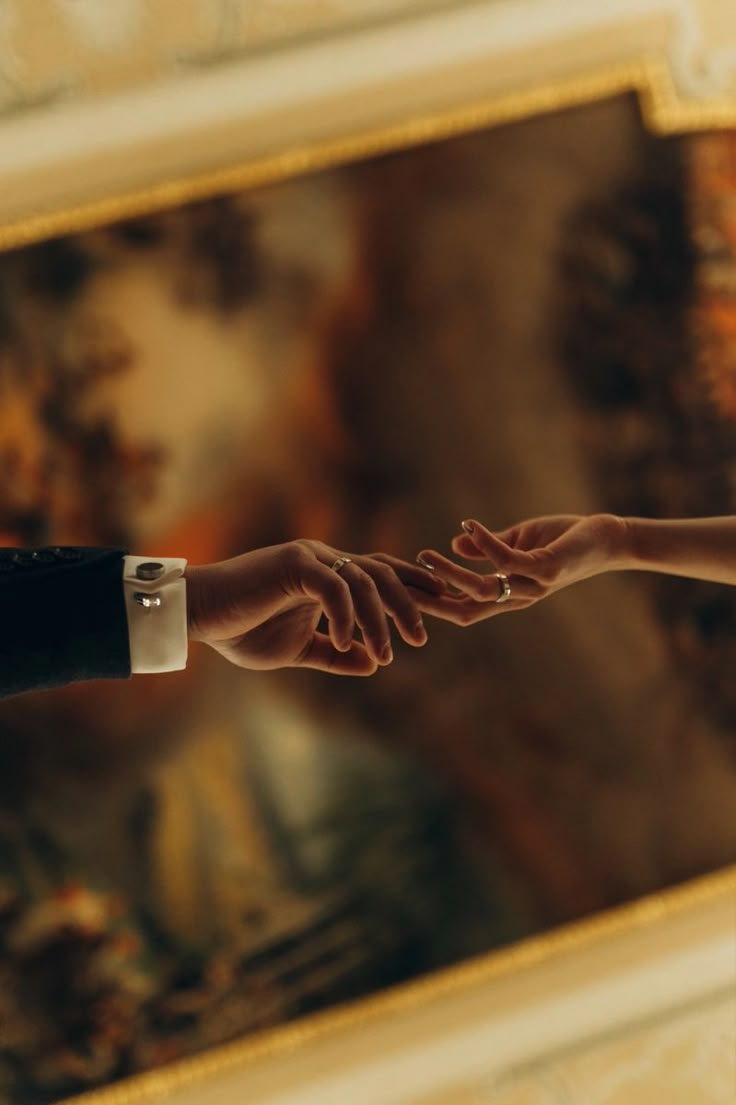 two people reaching out their hands to each other in front of a painting on the wall